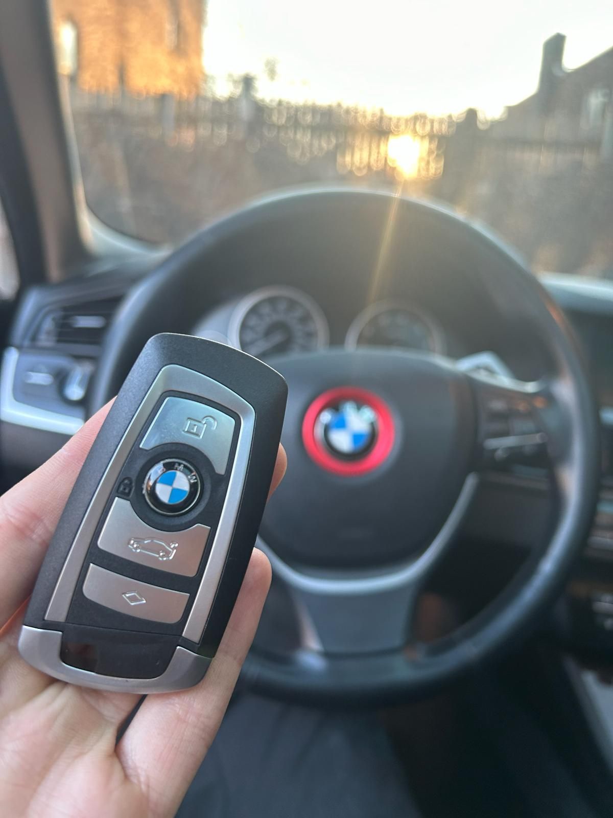 A person is holding a bmw key in front of a car steering wheel.