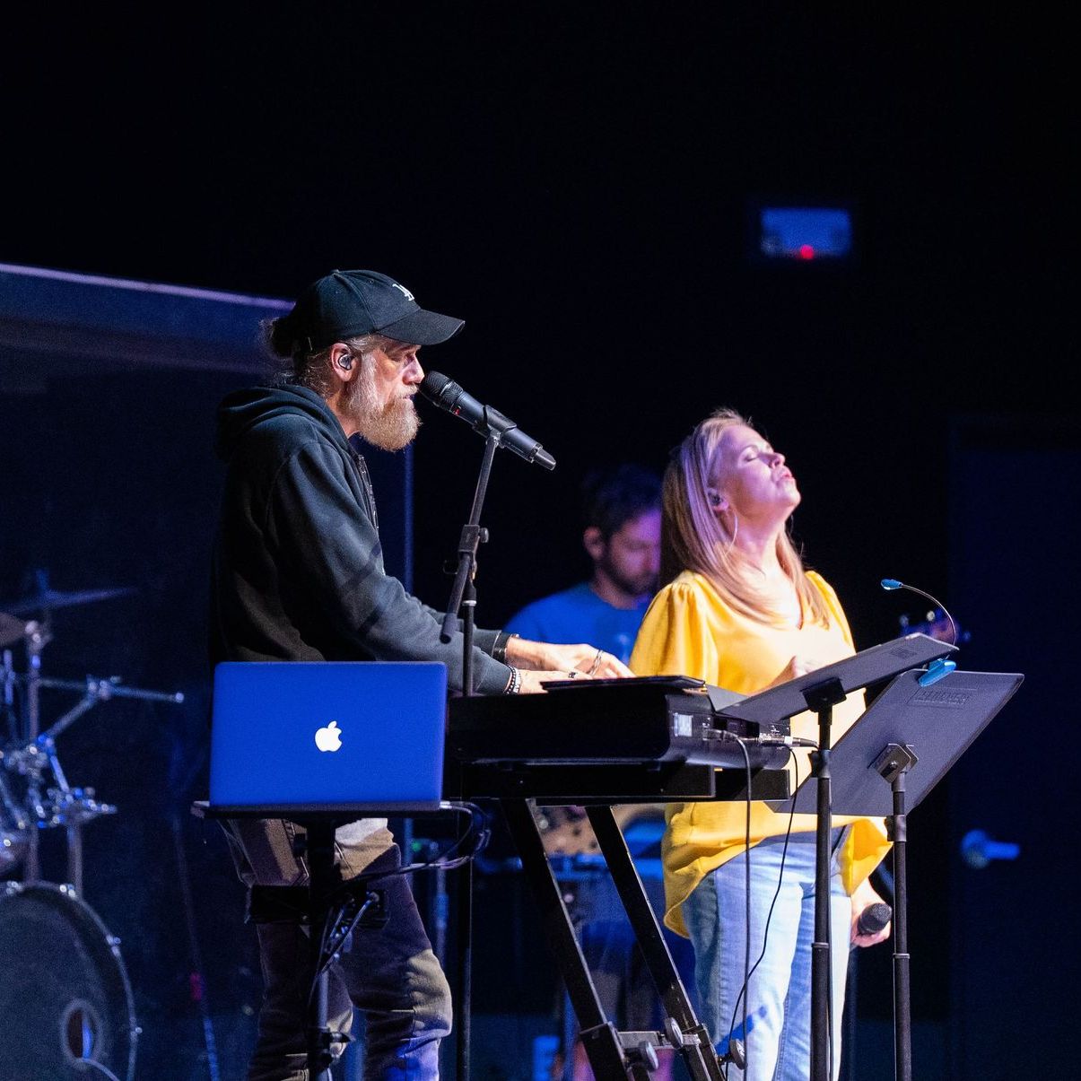 A man is playing a keyboard while a woman sings into a microphone.