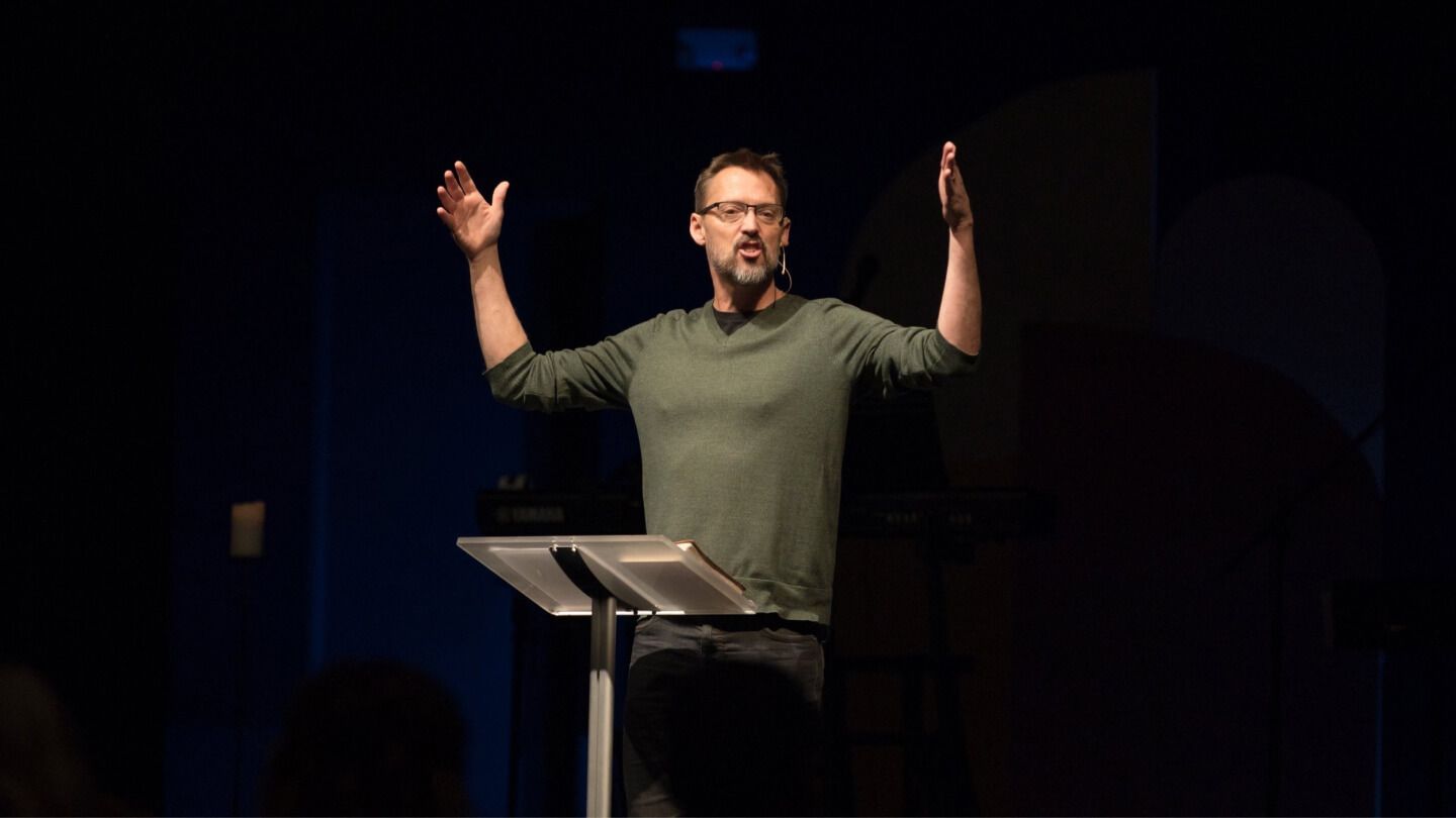A man is standing at a podium with his hands in the air.