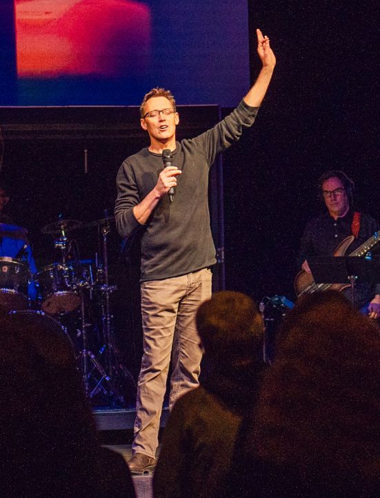 A man is standing on a stage holding a microphone and giving a speech.