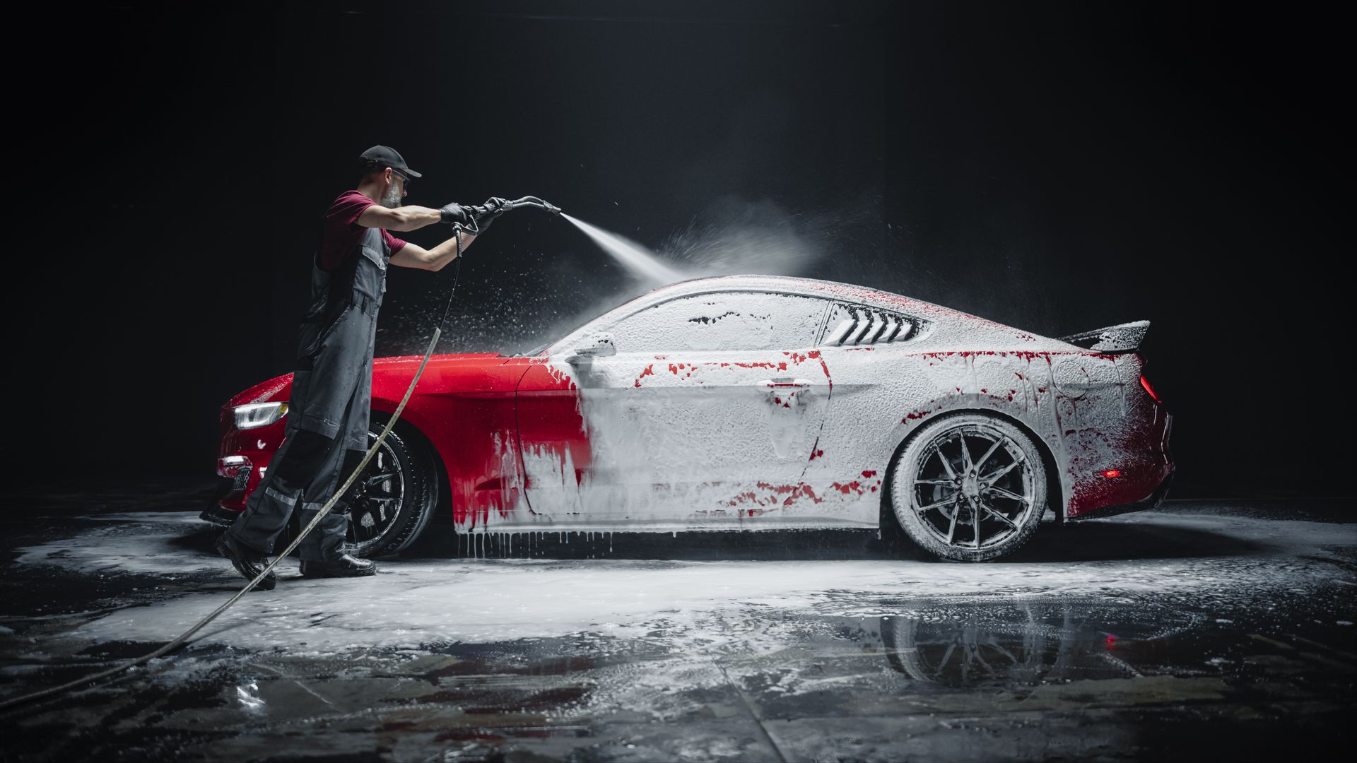 Person spraying foam over a red and white sports car in a dark car wash.