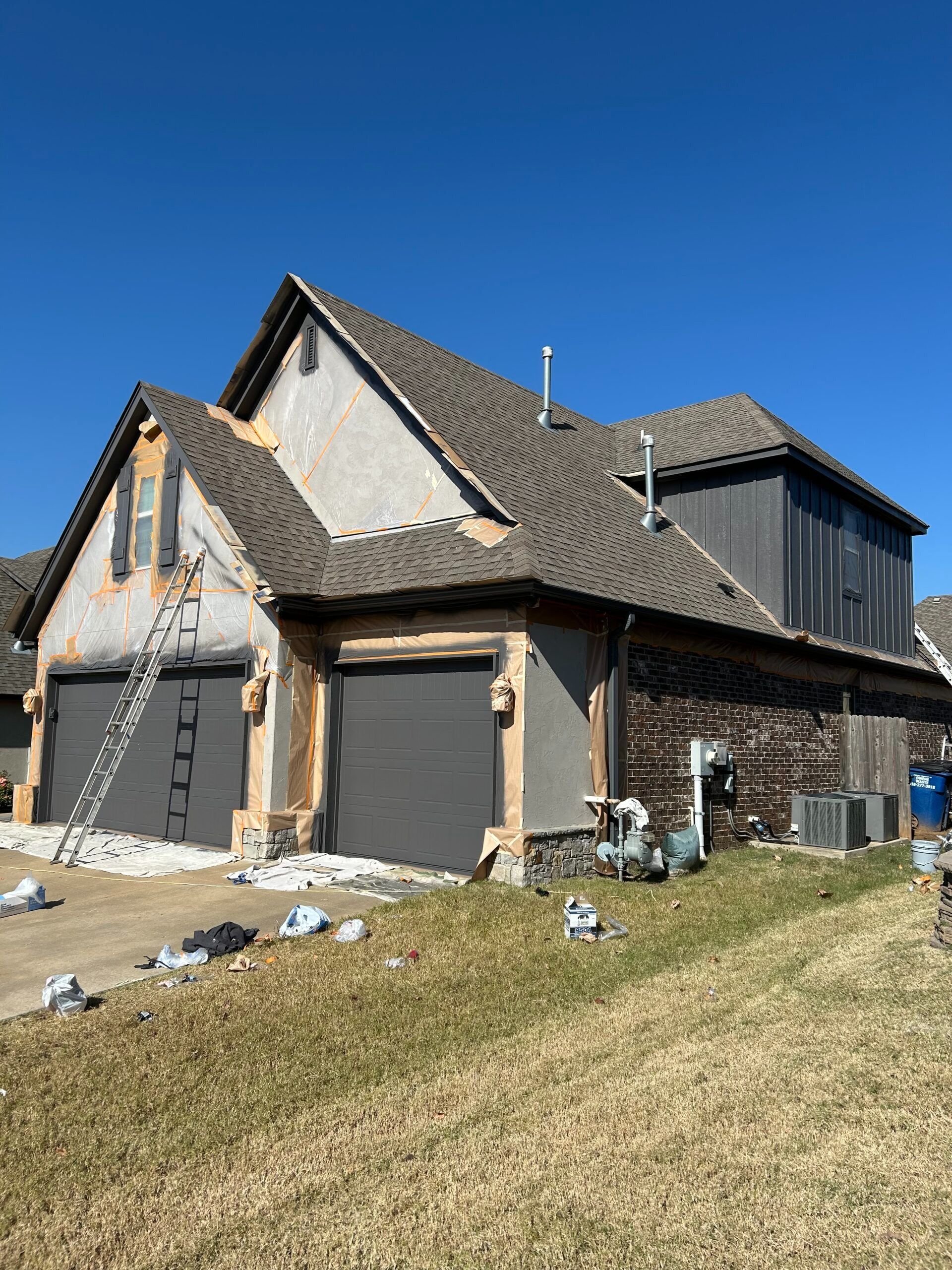 Partially built brick house with gray roof and construction materials on a grassy slope under a blue sky