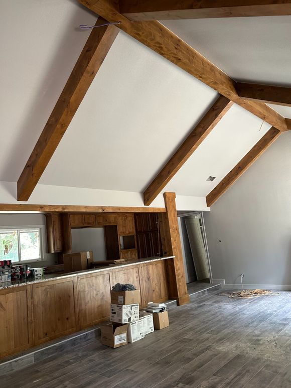 Rustic interior with exposed wood beams, a kitchen counter, and stacked boxes on a wooden floor.