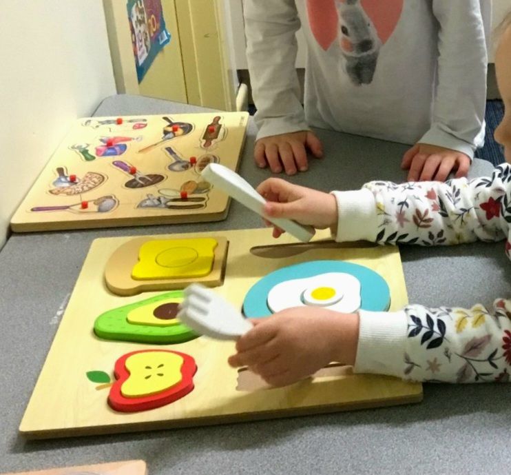 Two children are sitting at a table playing with glue.