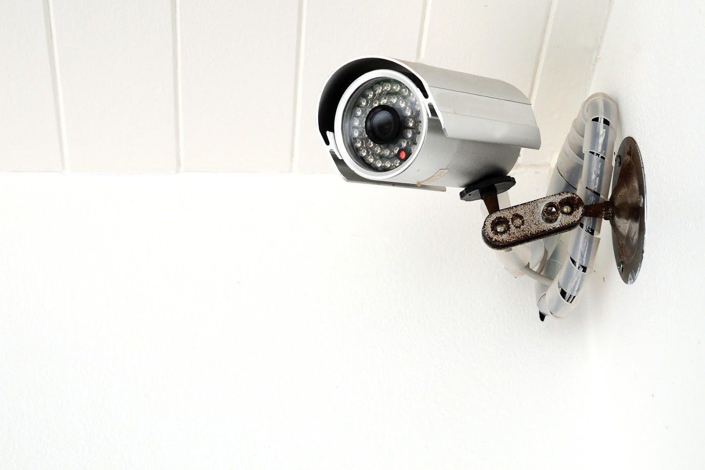 Silver security camera mounted on a white wall, pointing forward.