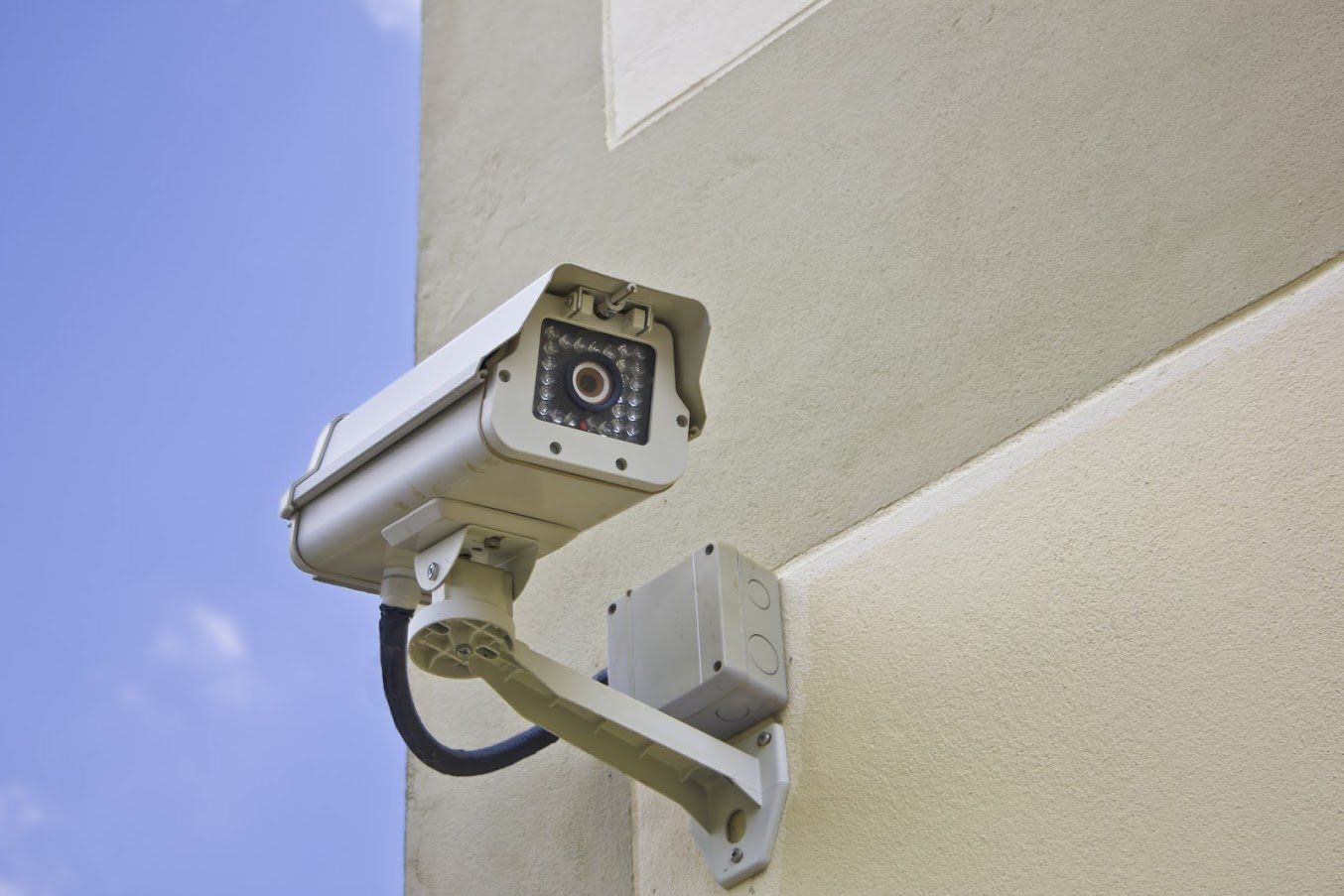 Security camera mounted on a beige building, blue sky background.