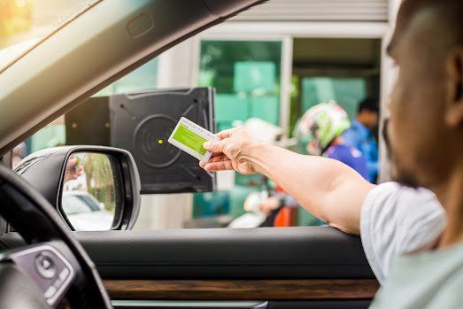 A person in a car reaching out to scan a green card at a toll booth.