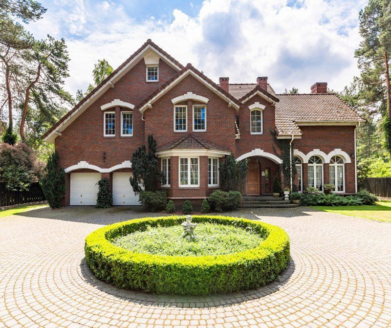 Brick home with a circular driveway. A fountain sits in the center of a hedge ring. The house has a detached two-car garage.