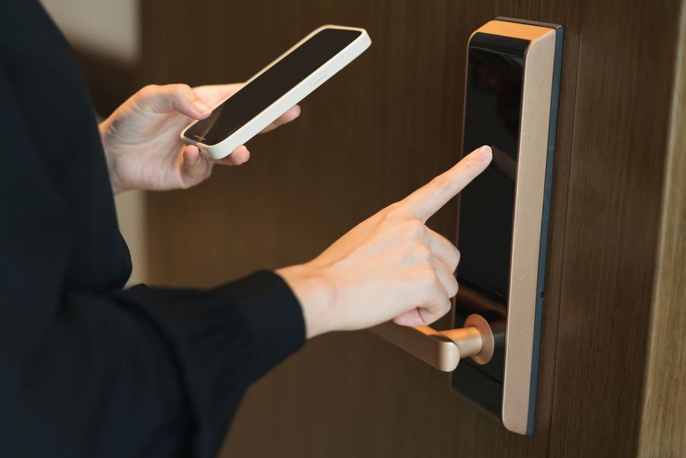 A person uses a smartphone and finger to unlock a smart door lock on a wooden door.