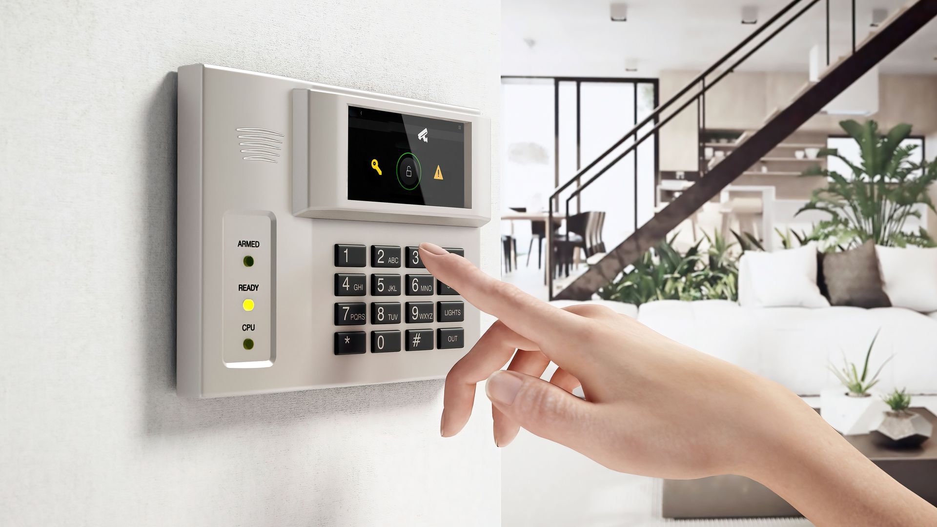 Hand entering code on a security system keypad mounted on a white wall; a modern living room is visible in the background.