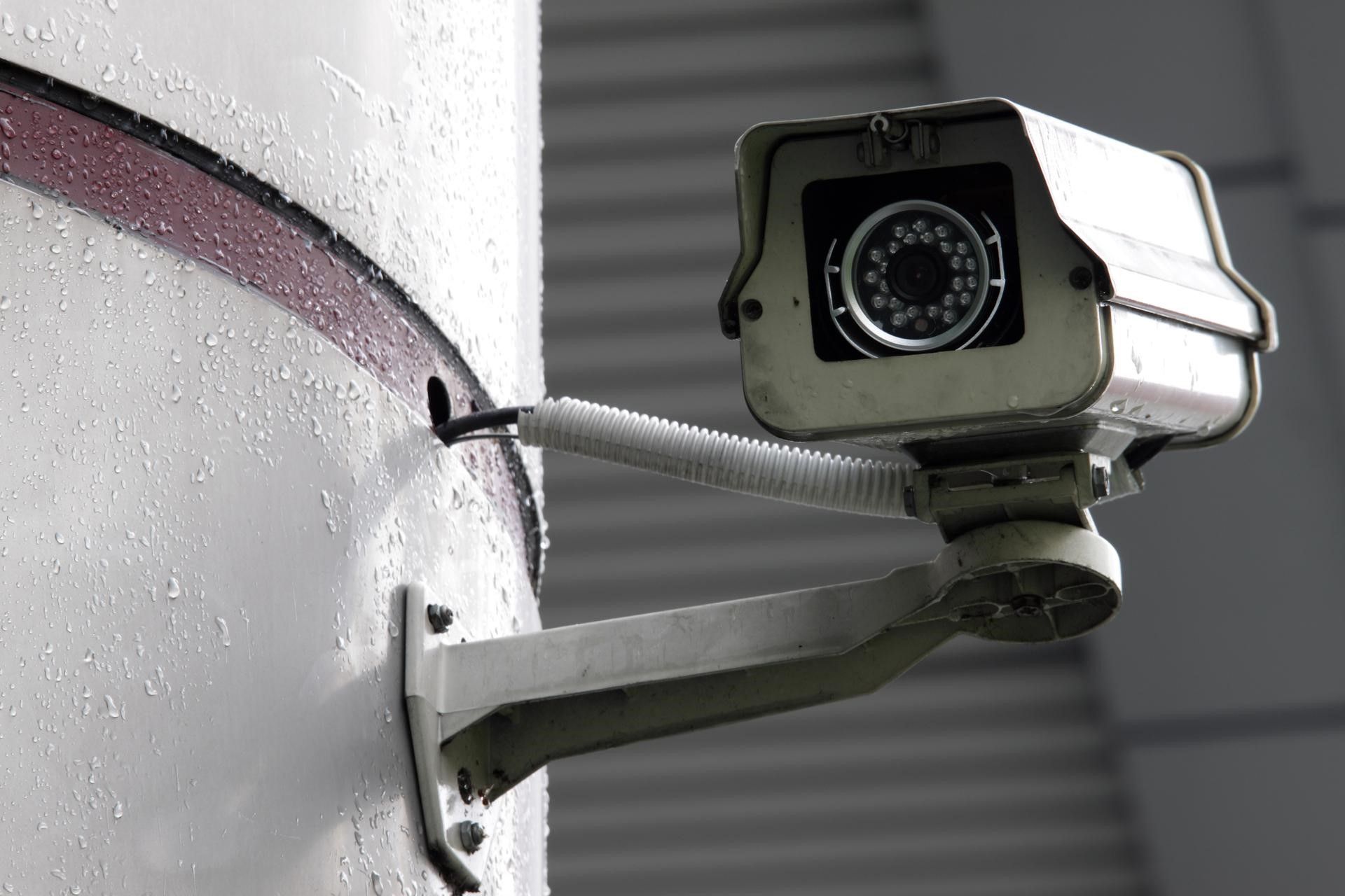 A security camera mounted on a pillar, with raindrops visible on its surface.