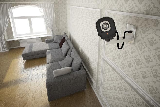 Interior view of a room with a gray couch, window, and a mounted security camera on patterned wallpaper.