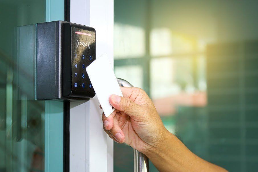 Hand holding white card near a black access card reader on a glass door.