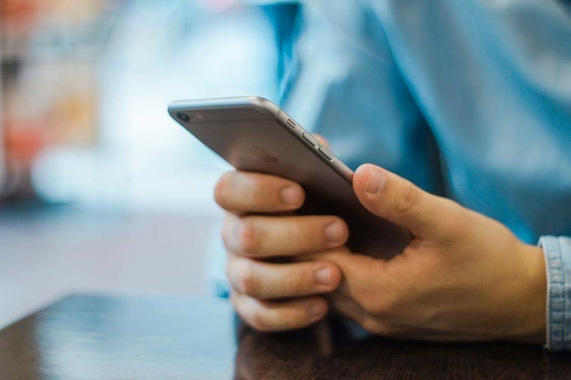 A person's hands holding a silver smartphone; they are wearing a blue shirt.