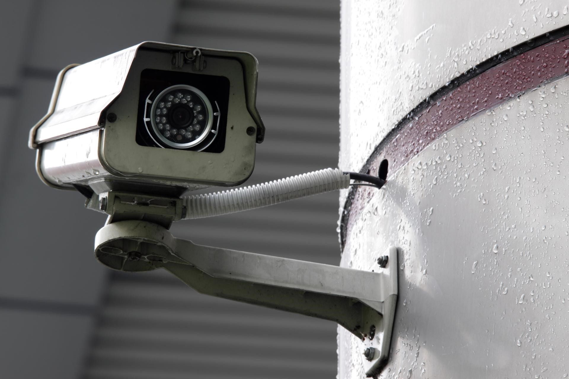 Security camera mounted on a white, possibly wet, cylindrical surface.