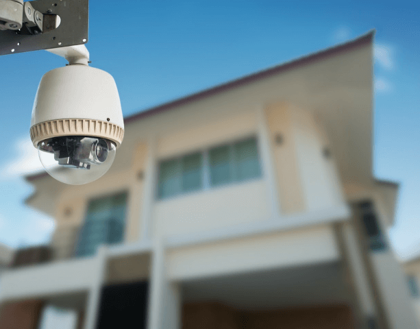 Security camera mounted outside a house, with a blurred background of the building and blue sky.