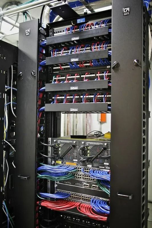 A server rack filled with lots of wires and cables. A server rack filled with network equipment, including switches, patch panels, and cabling; wires are color-coded.