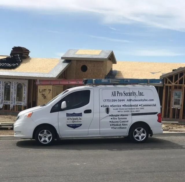 A white All Pro Security van parked in front of houses under construction. The van has company details and offers security services.