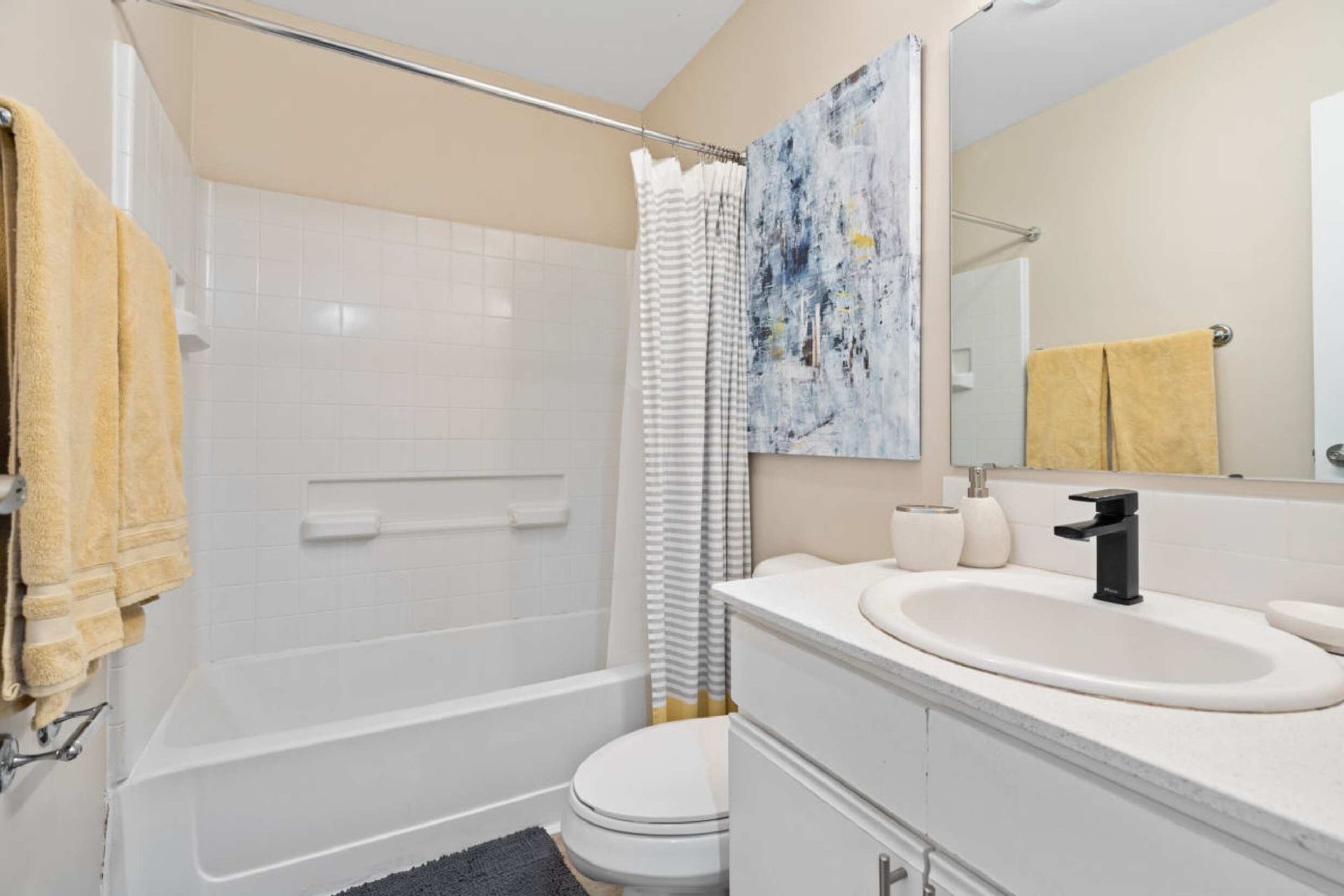 Bathroom with white tub, sink, and toilet. Yellow towels and abstract art.