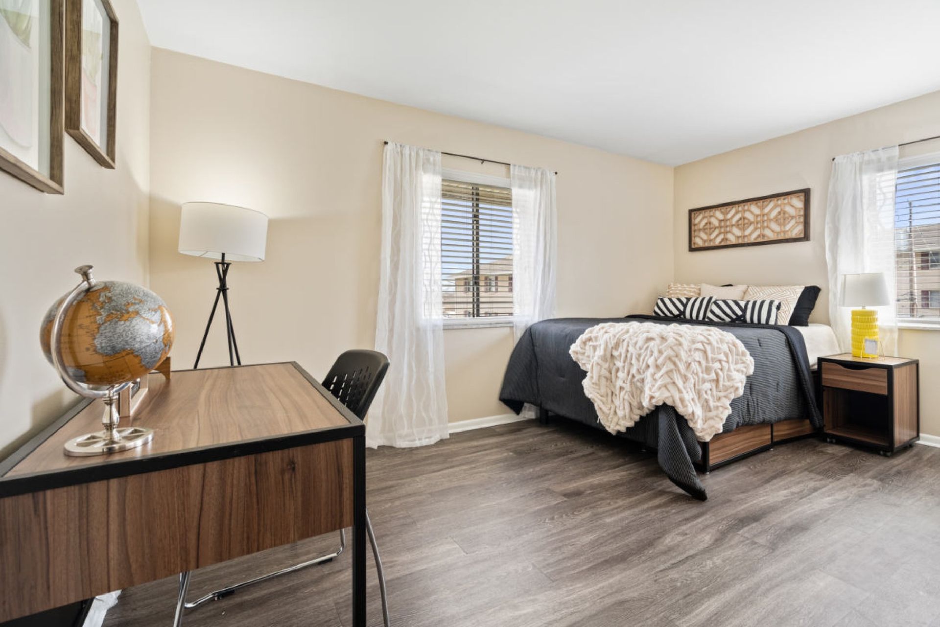 Bedroom with desk, bed, window, and globe. Neutral tones with dark bedspread and wood furniture.