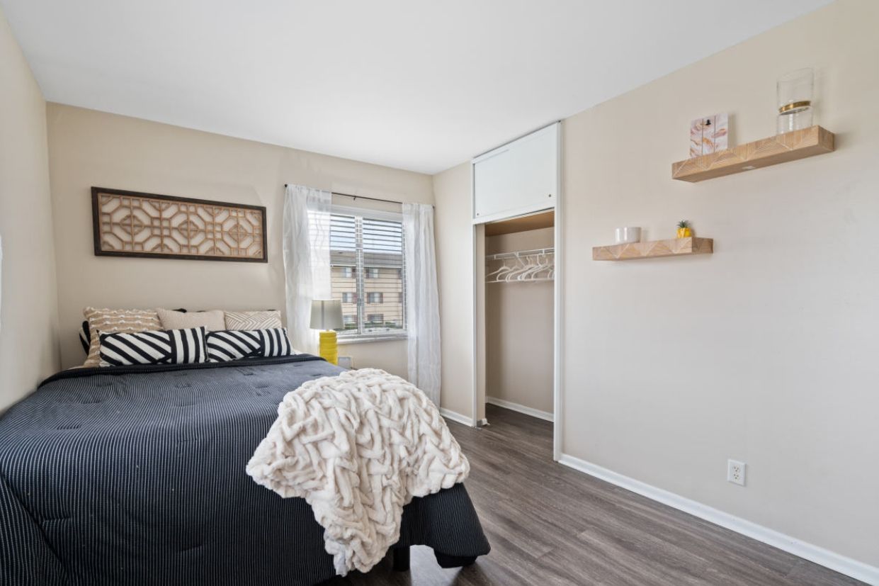 Bedroom with bed, window, closet, shelves, and neutral colors.