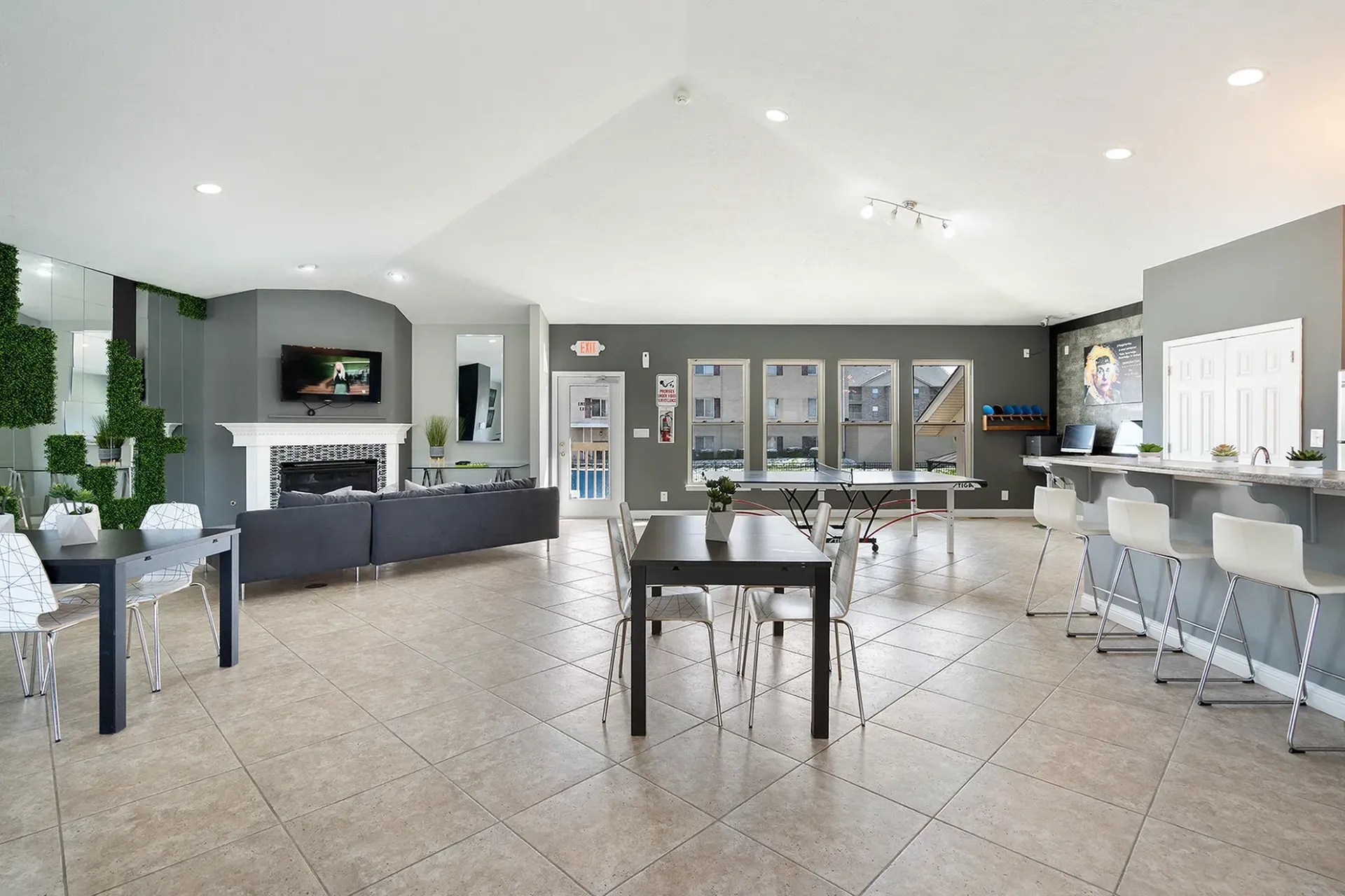 Bright, modern community space with tables, bar, display cases, fireplace, and artificial greenery.