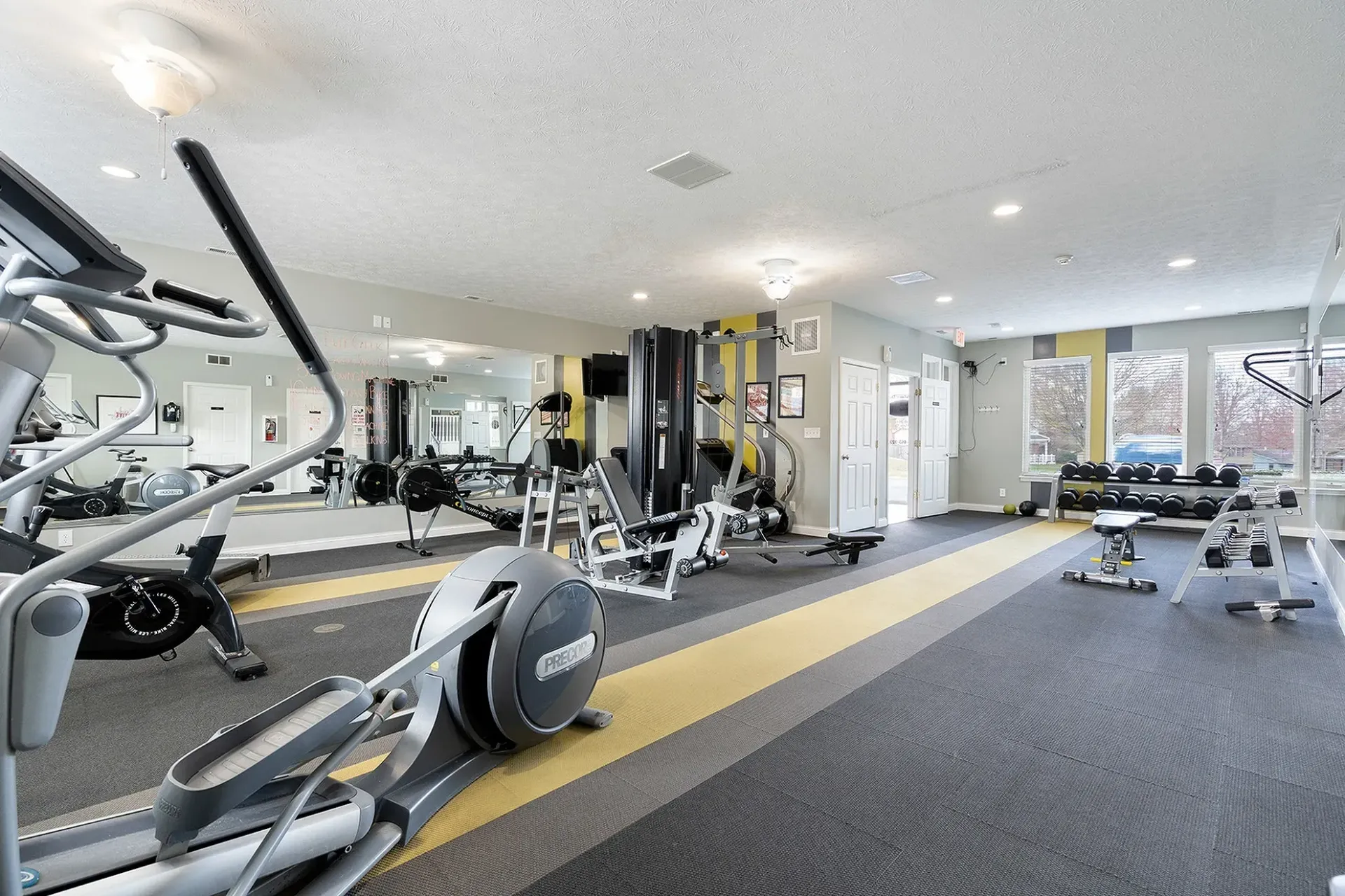 Gym with various exercise machines, including an elliptical, weights, and a bench.