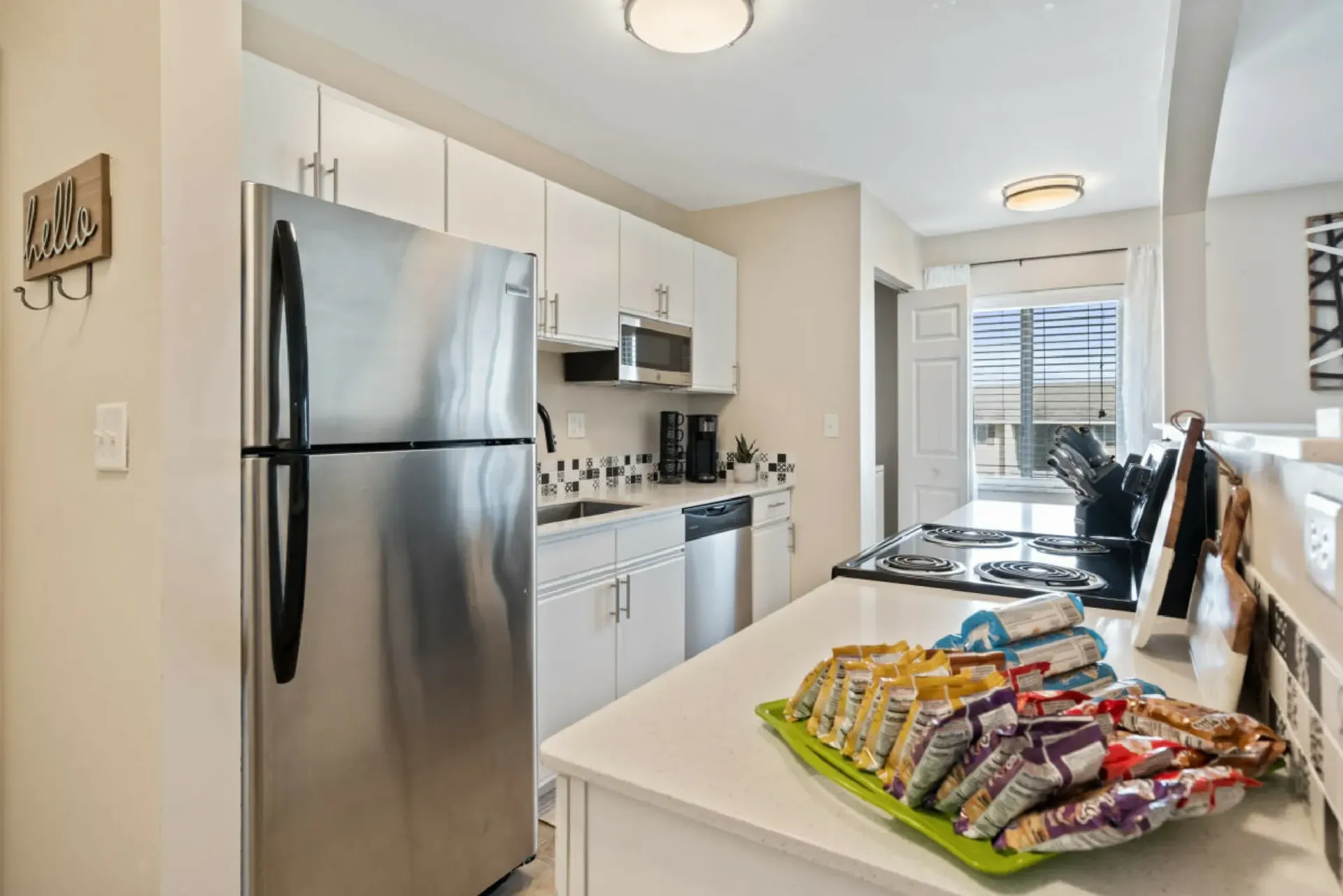 Kitchen with stainless steel refrigerator, white cabinets, and countertop with snacks; a window in the background.