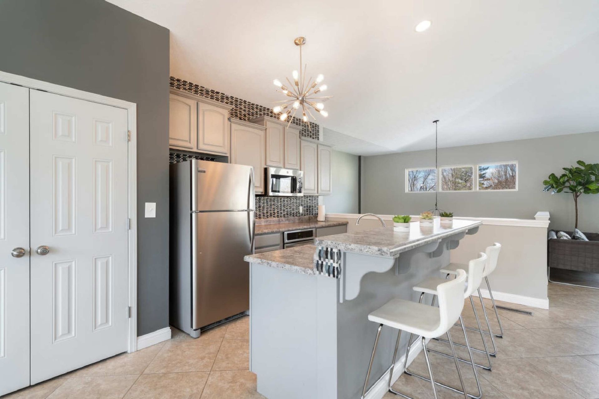 Modern kitchen with stainless steel appliances, a breakfast bar, and white bar stools.