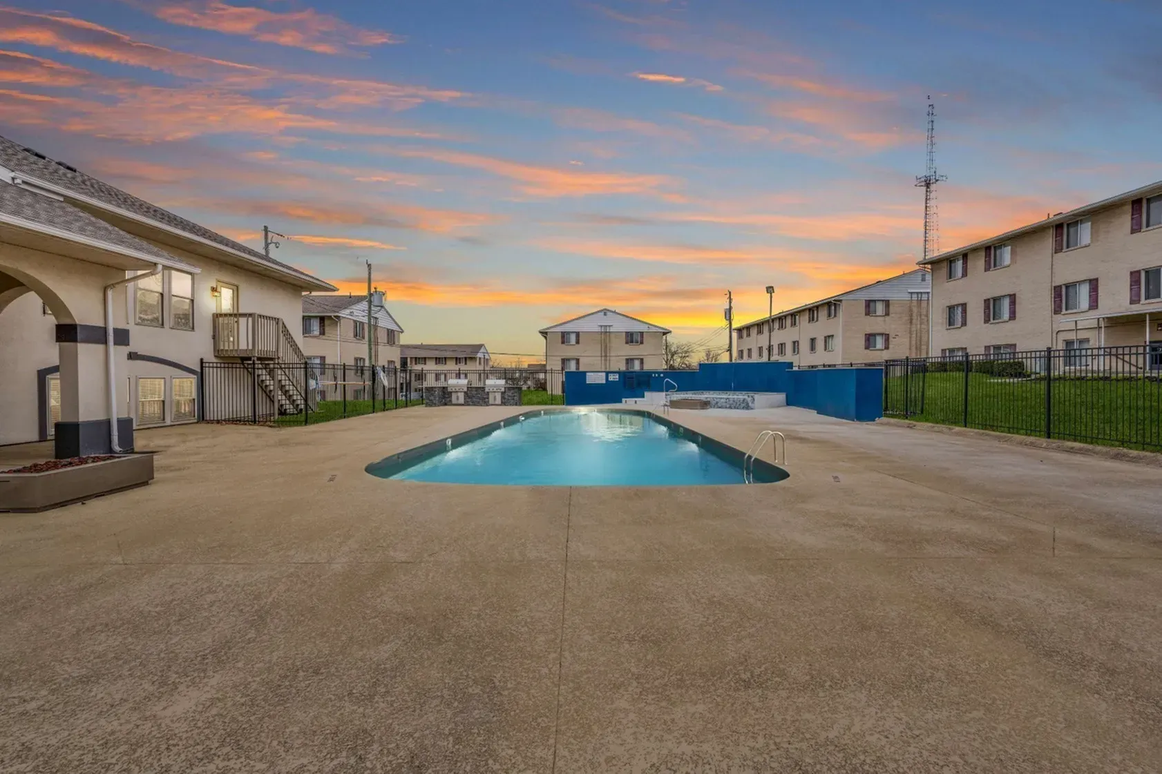 Apartment complex pool at sunset with surrounding buildings and sky.