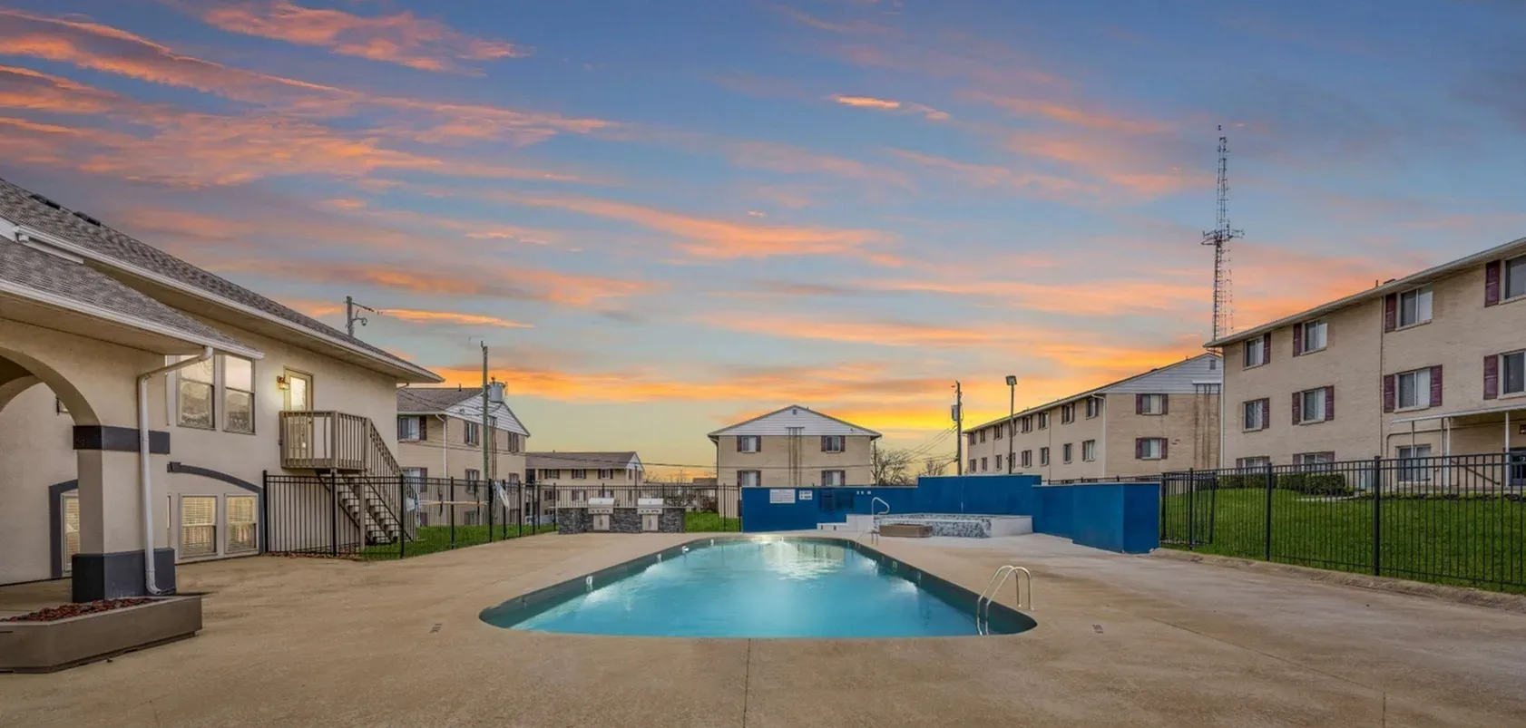 Apartment complex with a pool at dusk. Buildings, blue and orange sky, and a pool.