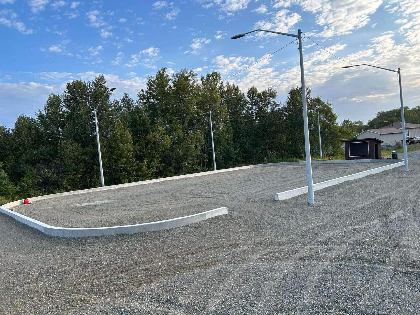 Une route de gravier avec des arbres en arrière-plan et un bâtiment en arrière-plan.