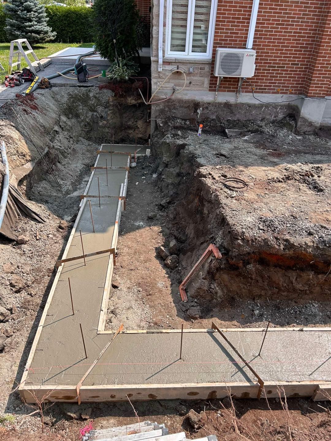 Une passerelle en béton est en cours de construction devant une maison en briques.