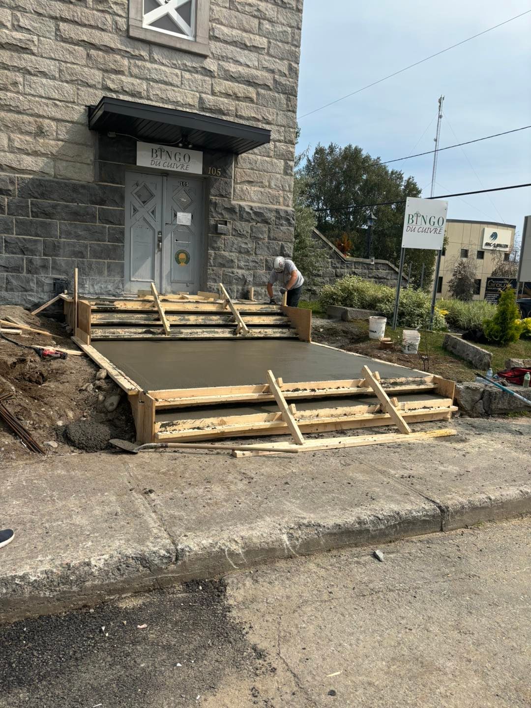 Un homme travaille sur une passerelle en béton devant un bâtiment en briques.