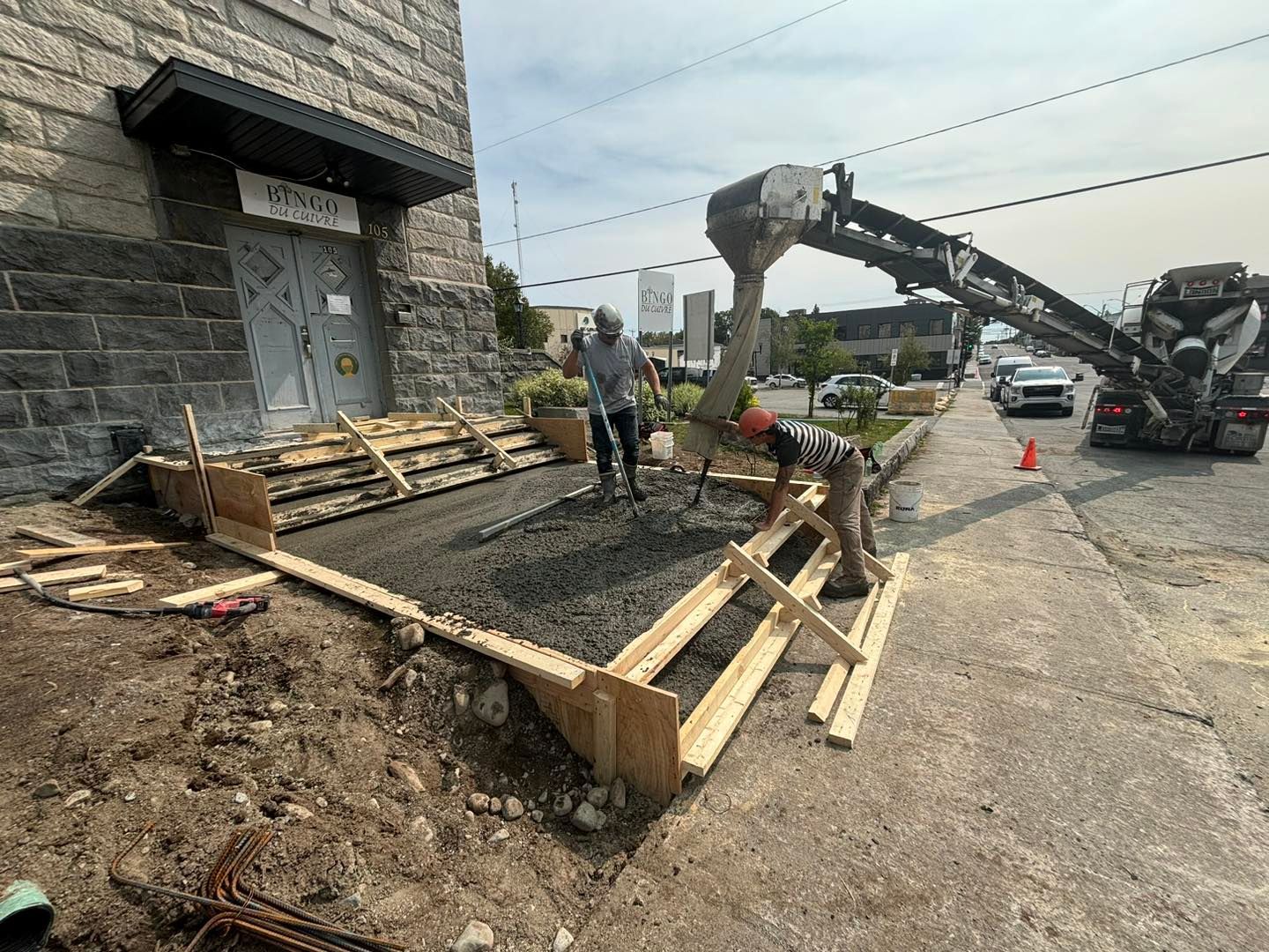 Un couple d'hommes travaille sur un trottoir devant un immeuble.