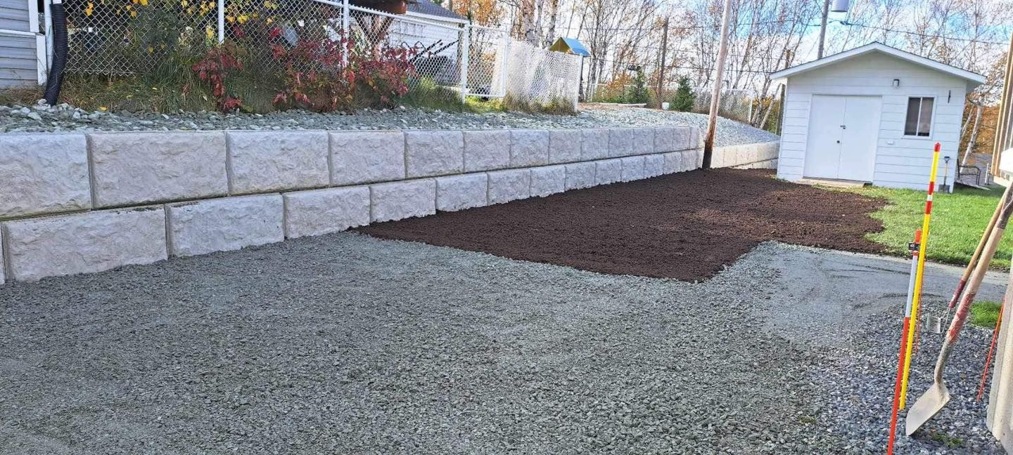 Une allée de gravier avec un mur de briques et un hangar en arrière-plan.