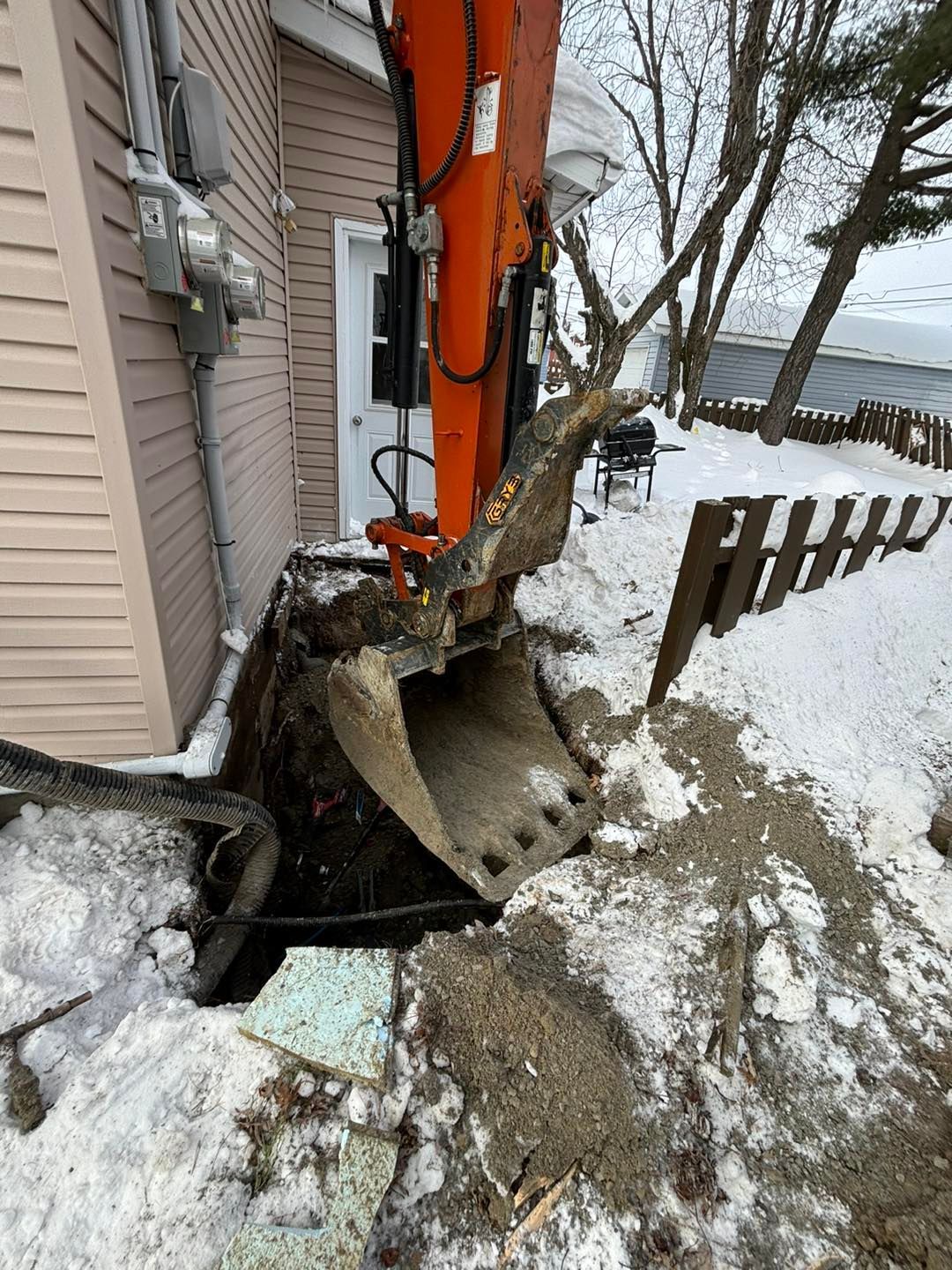 Une excavatrice creuse un trou sur le côté d'une maison.