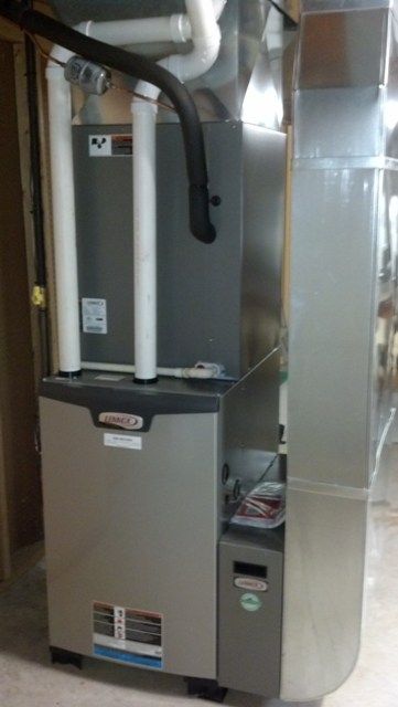 A gray air conditioner is sitting in a basement next to a wall.