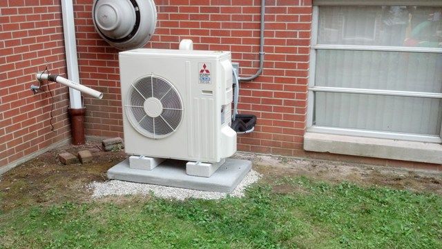 A mitsubishi air conditioner is sitting outside of a brick building.