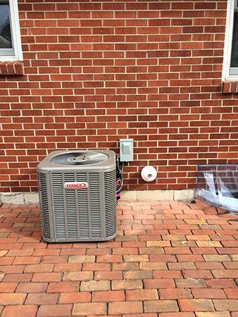 An air conditioner is sitting on a brick patio next to a brick wall.