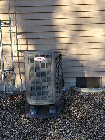 An air conditioner is sitting outside of a house next to a ladder.