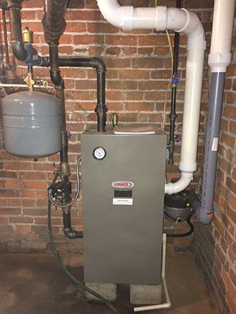 A stainless steel air conditioner is sitting next to a water heater in a basement.