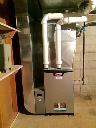 A boiler is sitting in a basement next to pipes.
