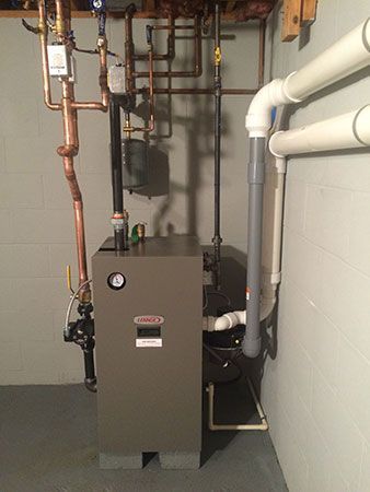 A boiler is sitting in a basement next to pipes.