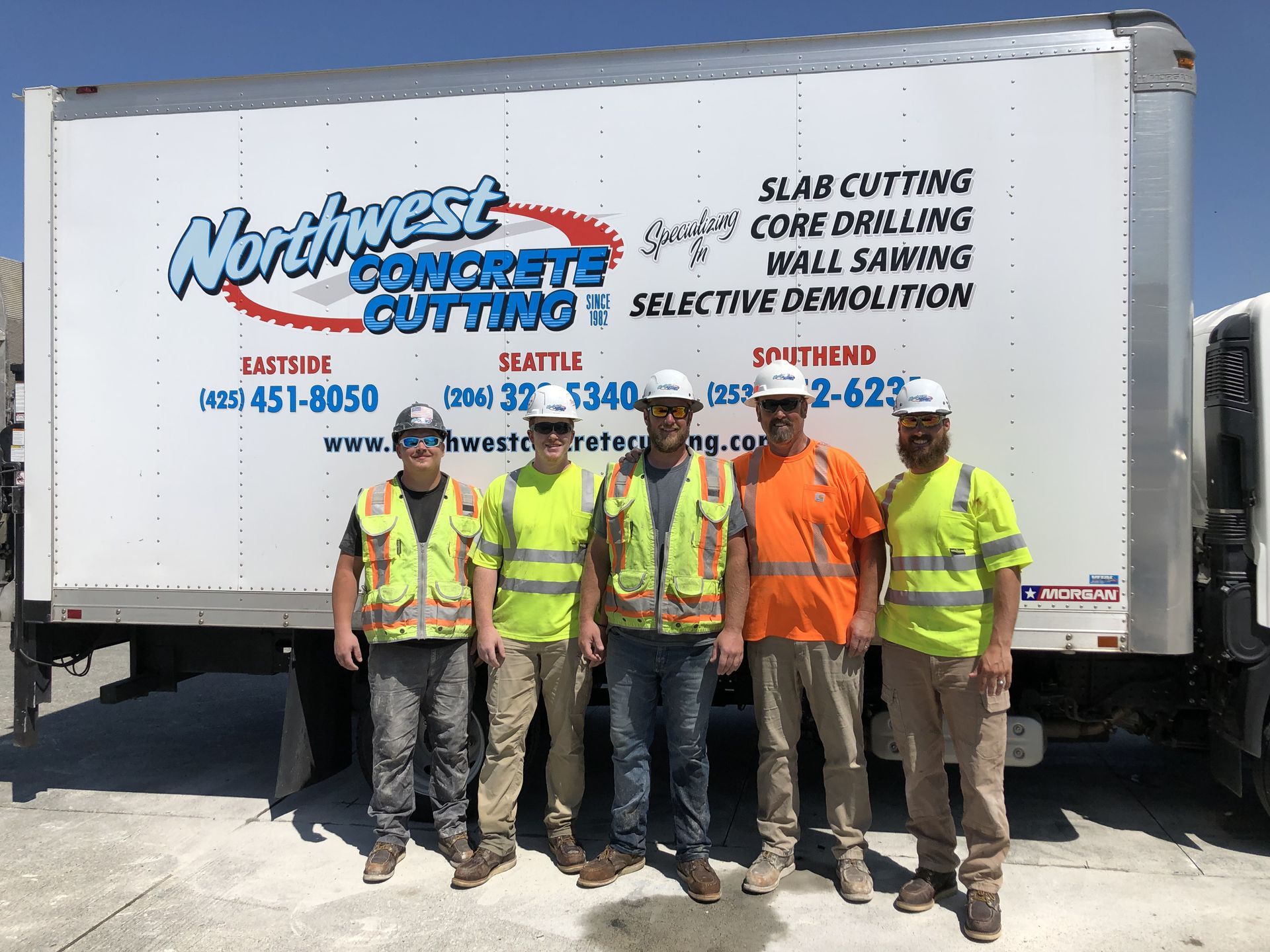 A group of construction workers are standing in front of a northwest concrete cutting truck.