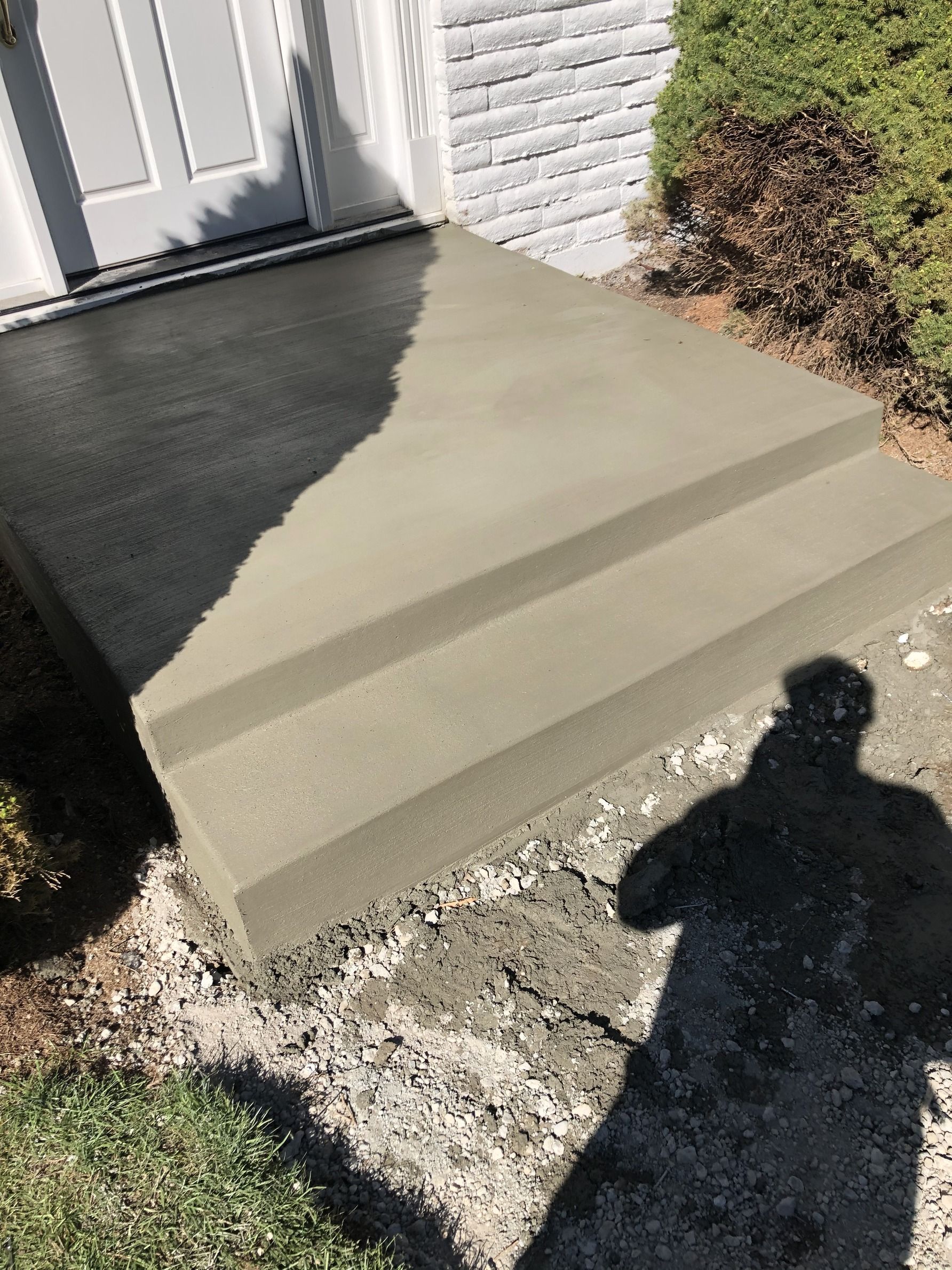 A shadow of a person is cast on a concrete staircase in front of a house.