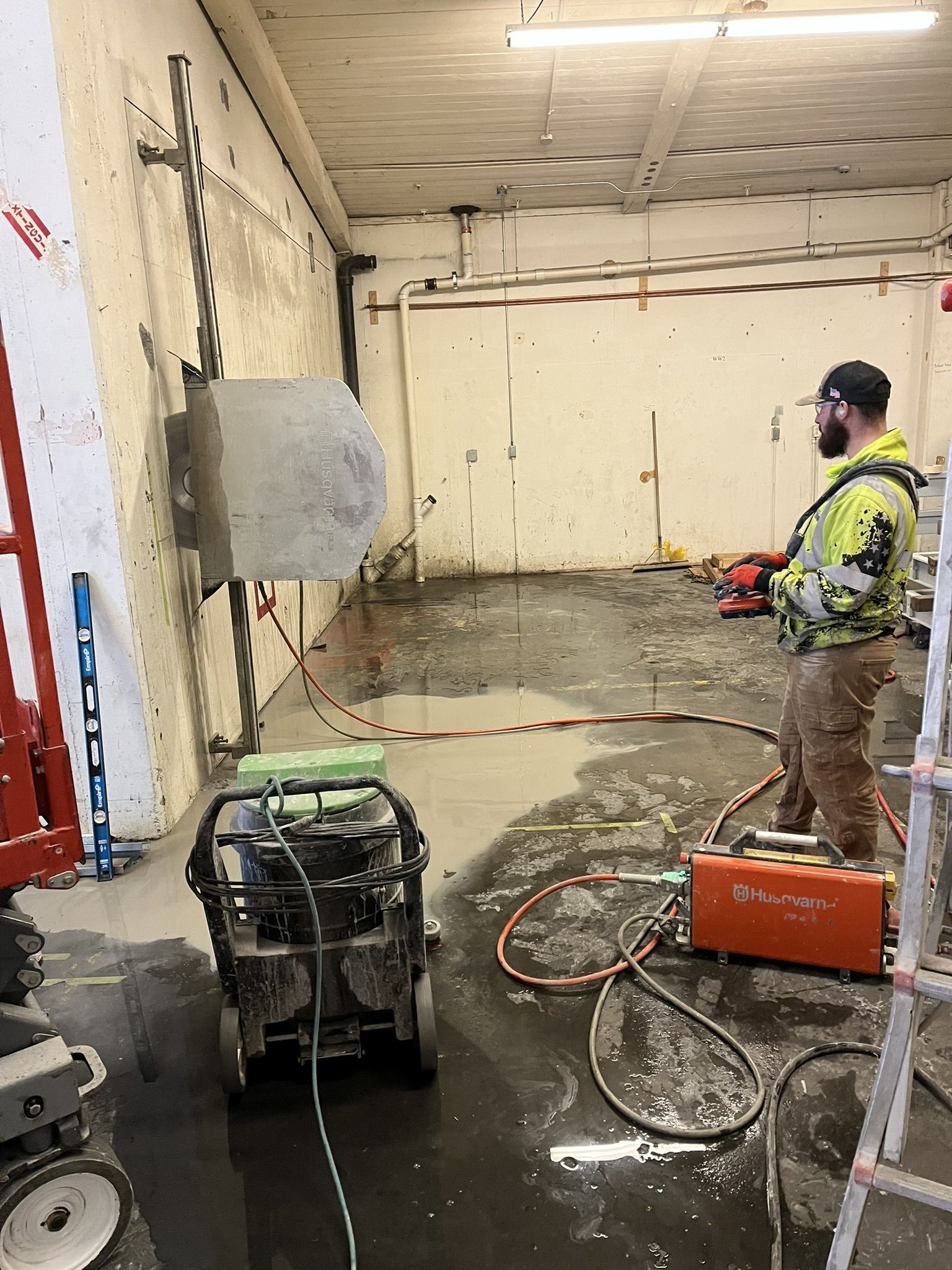 A man is standing in a room with a machine cutting a hole in the wall.