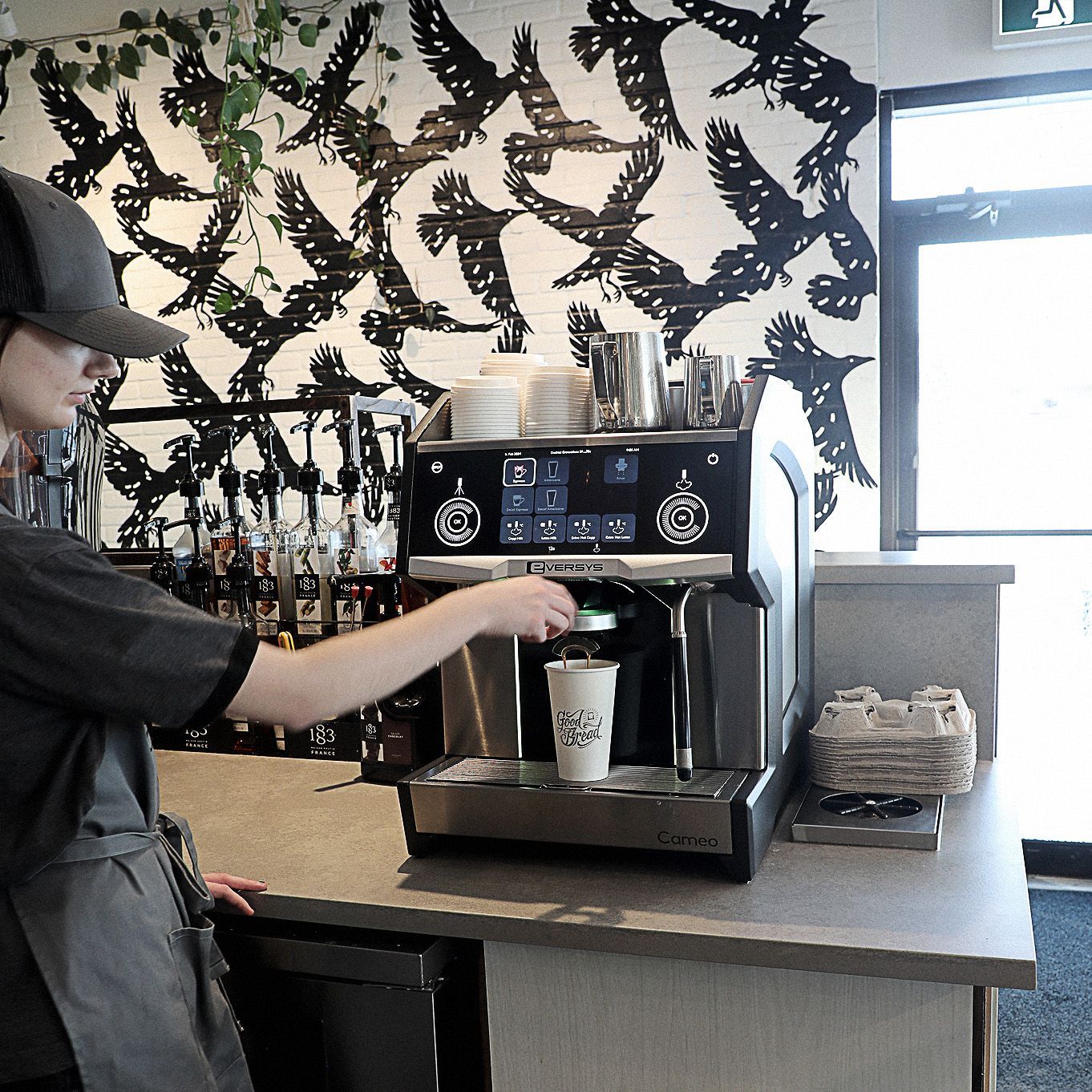 A man making a cup of coffee in front of a wall with birds on it