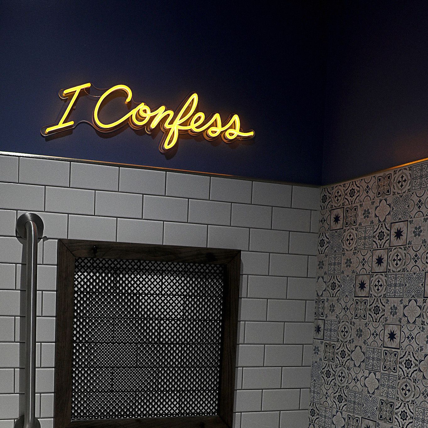 A bathroom with a neon sign that says i confess