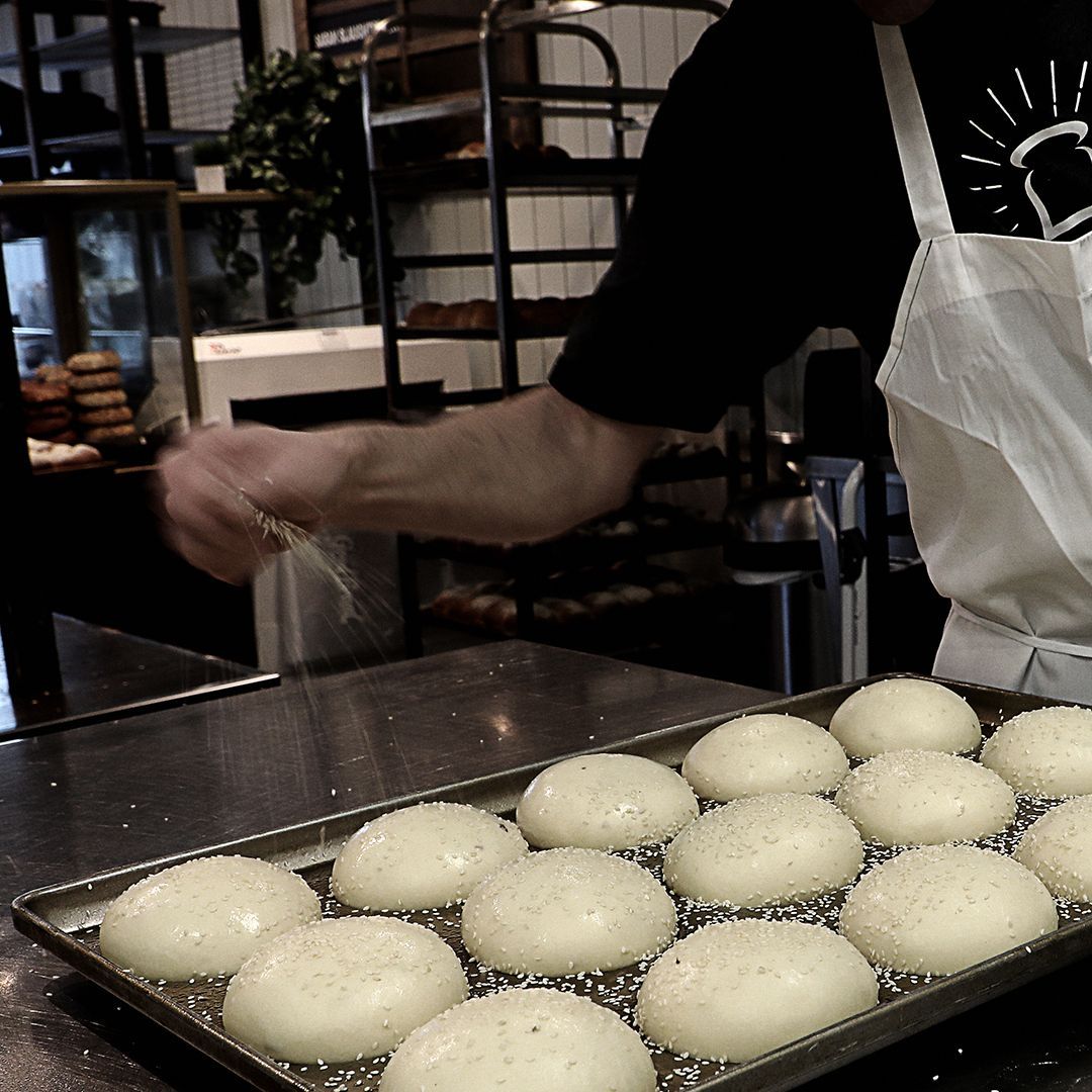 A man in an apron is working on a tray of dough